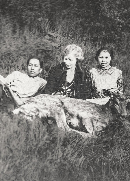 Vintage photo of three people sitting and posing in a field on tribal lands next to a deer that just had been hunted.